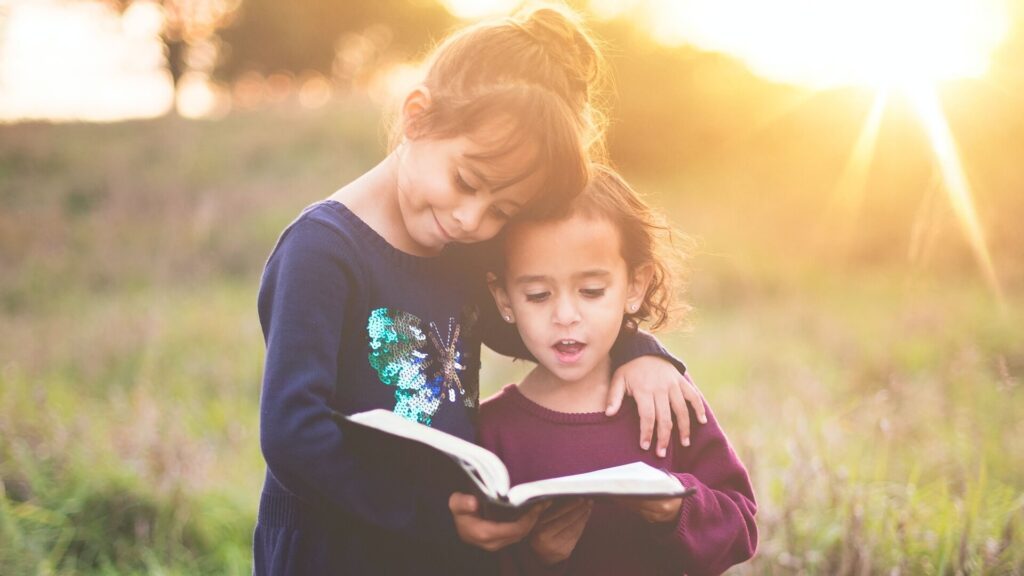 Duas crianças abraçadas leem um livro juntas enquanto o sol de poe atrás delas durante uma sessão fotografica.